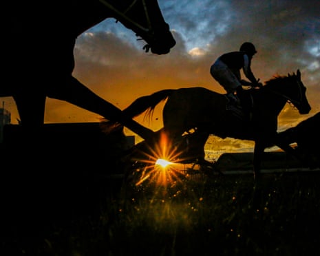 Silhouettes of racehorses and a jockey against a glowing sunset sky