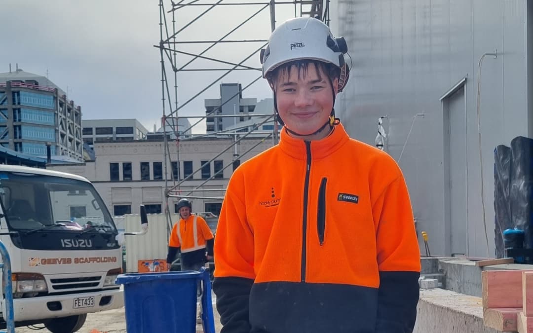 Bede Johnson, 18, standing in his hi-vis jacket and helmet at a construction worksite.