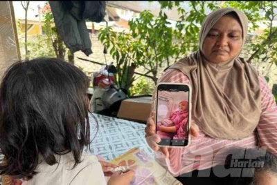 Anak sulung melihat gambar ibu mereka dalam telefon bimbit yang dipegang Marliza (kanan). FOTO: ADILA SHARINNI WAHID