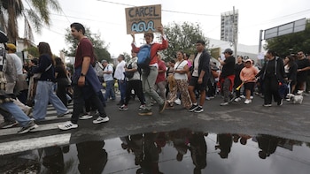 Personas caminan sobre el asfalto mojado en una marcha urbana mientras una de ellas sostiene una pancarta de cartón